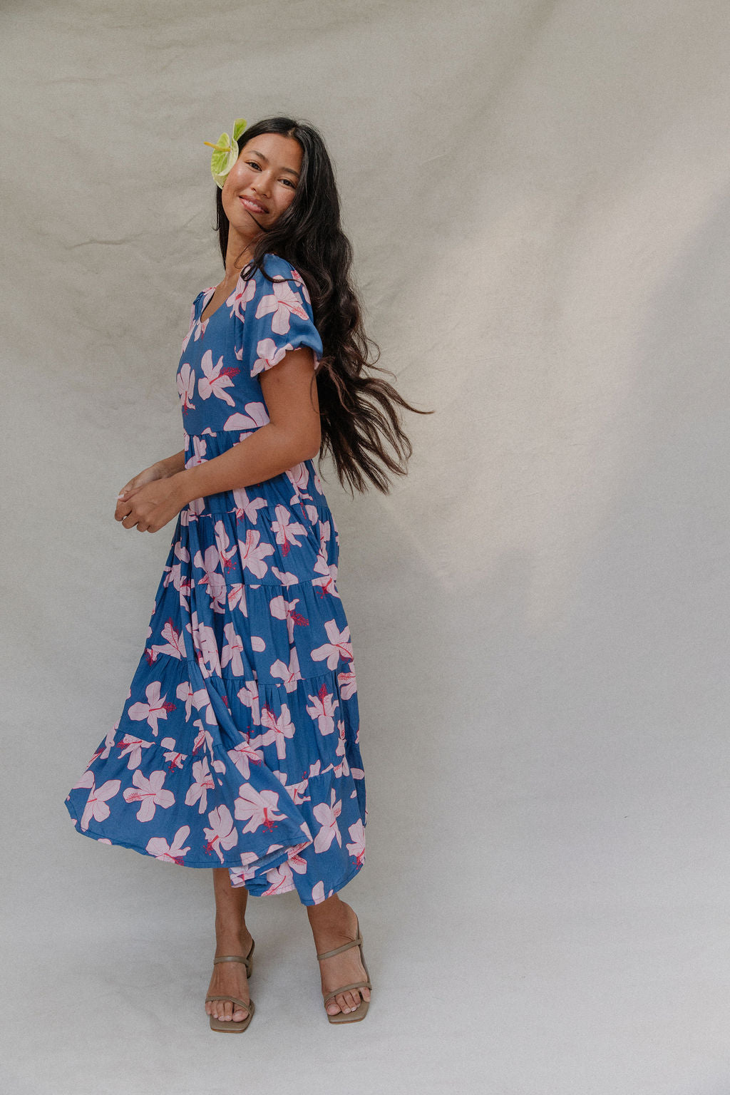 woman with brown hair wearing a navy scoop neck maxi dress with white hibiscus  print