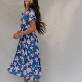 woman with brown hair wearing a navy scoop neck maxi dress with white hibiscus  print