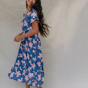 woman with brown hair wearing a navy scoop neck maxi dress with white hibiscus  print
