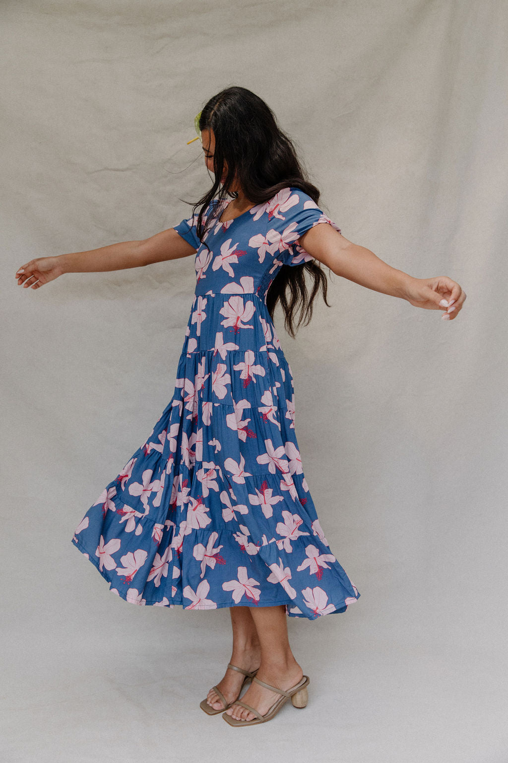 woman with brown hair wearing a navy scoop neck maxi dress with white hibiscus  print