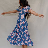 woman with brown hair wearing a navy scoop neck maxi dress with white hibiscus  print