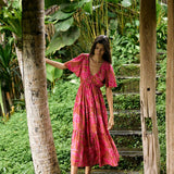 Woman with dark hair wearing tiered maxi dress with sleeves. It is the Mariana Dress in the Garden 'Awapuhi print. 