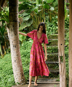 Woman with dark hair wearing tiered maxi dress with sleeves. It is the Mariana Dress in the Garden 'Awapuhi print. 