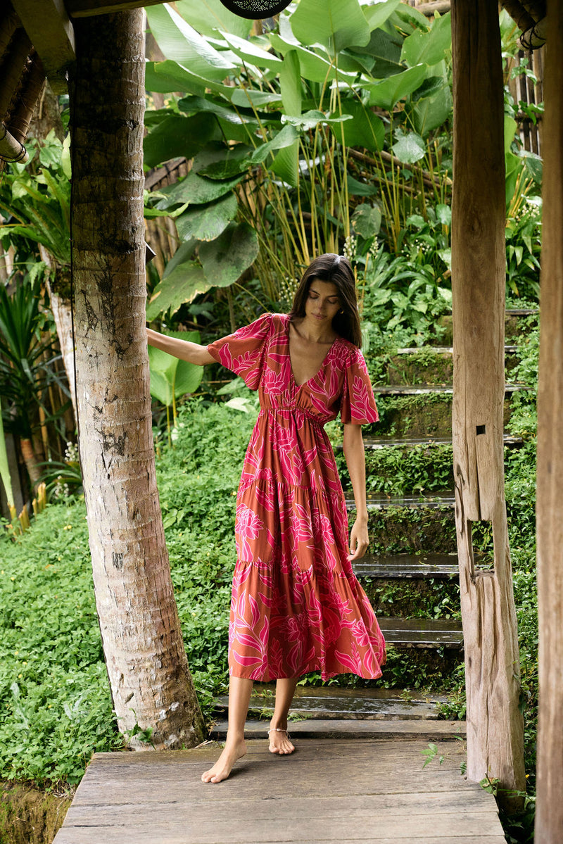 Woman with dark hair wearing tiered maxi dress with sleeves. It is the Mariana Dress in the Garden 'Awapuhi print. 