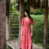 Woman with dark hair wearing tiered maxi dress with sleeves. It is the Mariana Dress in the Garden 'Awapuhi print. 