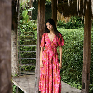 Woman with dark hair wearing tiered maxi dress with sleeves. It is the Mariana Dress in the Garden 'Awapuhi print. 