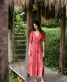 Woman with dark hair wearing tiered maxi dress with sleeves. It is the Mariana Dress in the Garden 'Awapuhi print. 