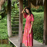 Woman with dark hair wearing tiered maxi dress with sleeves. It is the Mariana Dress in the Garden 'Awapuhi print. 