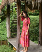 Woman with dark hair wearing tiered maxi dress with sleeves. It is the Mariana Dress in the Garden 'Awapuhi print. 