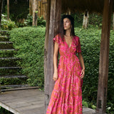 Woman with dark hair wearing tiered maxi dress with sleeves. It is the Mariana Dress in the Garden 'Awapuhi print. 