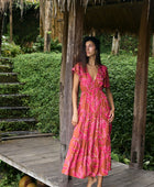 Woman with dark hair wearing tiered maxi dress with sleeves. It is the Mariana Dress in the Garden 'Awapuhi print. 