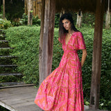 Woman with dark hair wearing tiered maxi dress with sleeves. It is the Mariana Dress in the Garden 'Awapuhi print. 