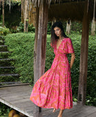 Woman with dark hair wearing tiered maxi dress with sleeves. It is the Mariana Dress in the Garden 'Awapuhi print. 