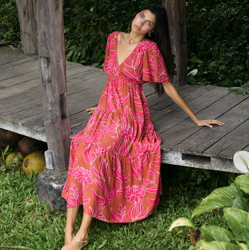 Woman with dark hair wearing tiered maxi dress with sleeves. It is the Mariana Dress in the Garden 'Awapuhi print. 