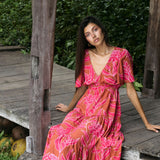 Woman with dark hair wearing tiered maxi dress with sleeves. It is the Mariana Dress in the Garden 'Awapuhi print. 