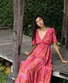 Woman with dark hair wearing tiered maxi dress with sleeves. It is the Mariana Dress in the Garden 'Awapuhi print. 