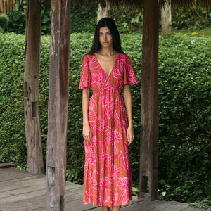 Woman with dark hair wearing tiered maxi dress with sleeves. It is the Mariana Dress in the Garden 'Awapuhi print. 