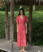 Woman with dark hair wearing tiered maxi dress with sleeves. It is the Mariana Dress in the Garden 'Awapuhi print. 