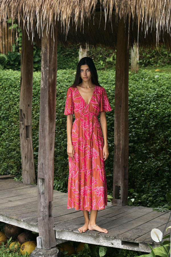 Woman with dark hair wearing tiered maxi dress with sleeves. It is the Mariana Dress in the Garden 'Awapuhi print. 