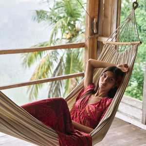 Woman with dark hair wearing tiered maxi dress with sleeves. It is the Mariana Dress in the Garden 'Awapuhi print. 