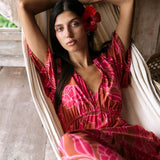 Woman with dark hair wearing tiered maxi dress with sleeves. It is the Mariana Dress in the Garden 'Awapuhi print. 