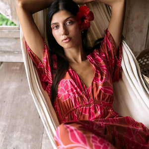 Woman with dark hair wearing tiered maxi dress with sleeves. It is the Mariana Dress in the Garden 'Awapuhi print. 
