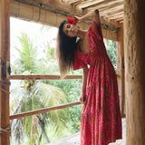 Woman with dark hair wearing tiered maxi dress with sleeves. It is the Mariana Dress in the Garden 'Awapuhi print. 