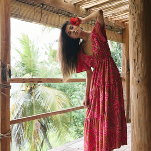 Woman with dark hair wearing tiered maxi dress with sleeves. It is the Mariana Dress in the Garden 'Awapuhi print. 