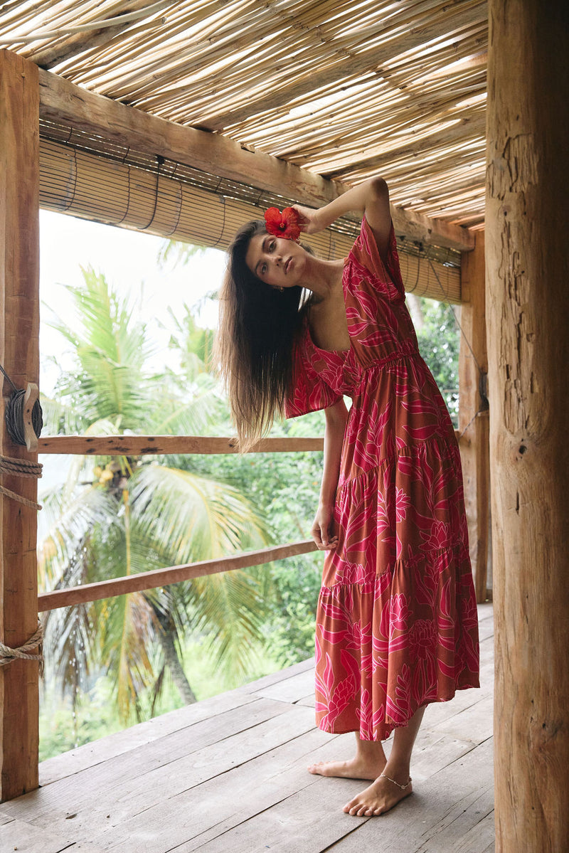 Woman with dark hair wearing tiered maxi dress with sleeves. It is the Mariana Dress in the Garden 'Awapuhi print. 