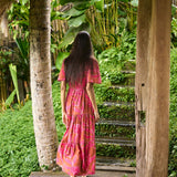Woman with dark hair wearing tiered maxi dress with sleeves. It is the Mariana Dress in the Garden 'Awapuhi print. 