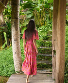 Woman with dark hair wearing tiered maxi dress with sleeves. It is the Mariana Dress in the Garden 'Awapuhi print. 