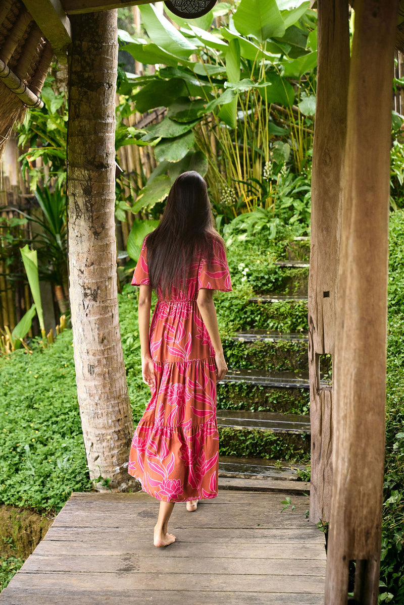 Woman with dark hair wearing tiered maxi dress with sleeves. It is the Mariana Dress in the Garden 'Awapuhi print. 