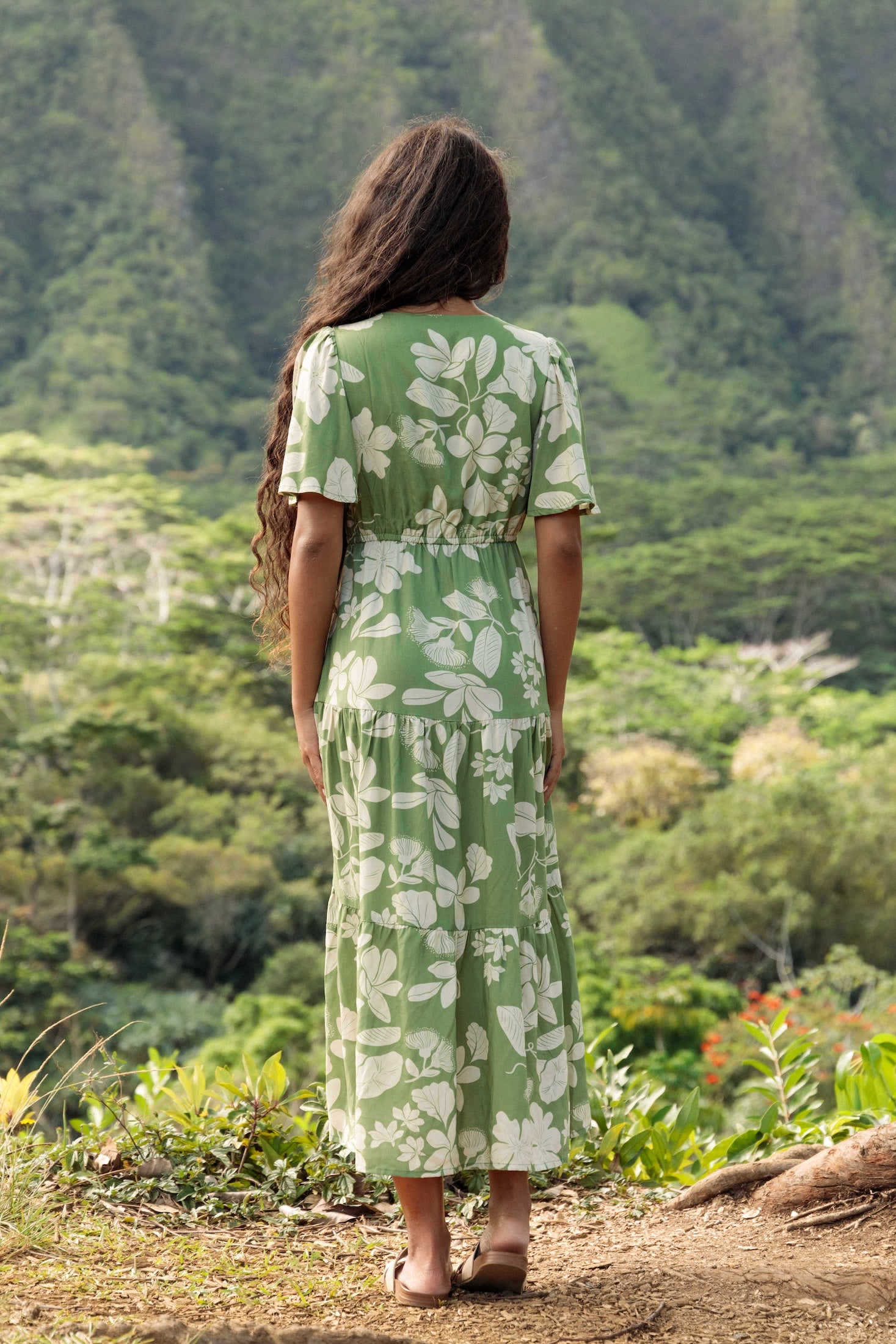 woman with brown hair wearing green v neck maxi dress with native Hawaiian plants 