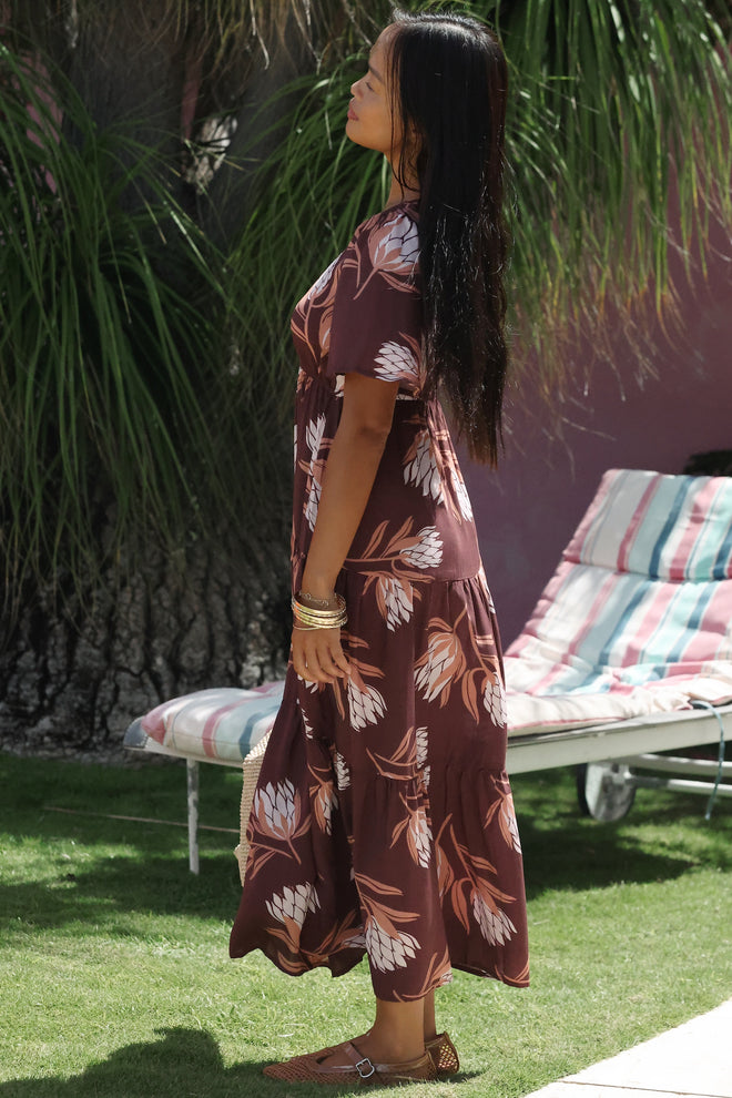 woman wearing brown maxi, v-neck, flutter sleeve dress with protea print