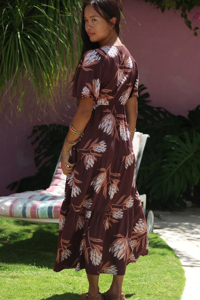 woman wearing brown maxi, v-neck, flutter sleeve dress with protea print