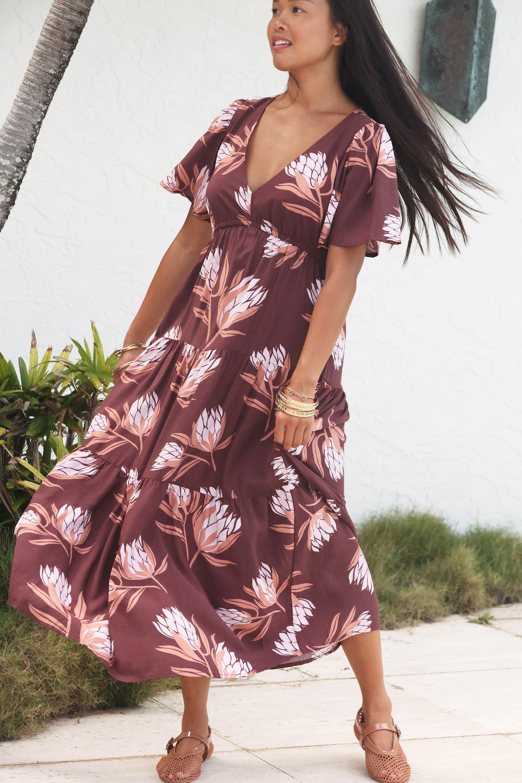 woman wearing brown maxi, v-neck, flutter sleeve dress with protea print