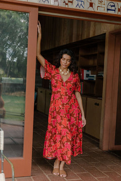 woman with brown hair wearing a maxi v-neck dress with flutter sleeve in a vibrant pink pua pattern