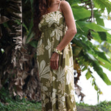 woman with brown hair wearing a maxi flowy dress in a green color with naupaka pattern throughout. 