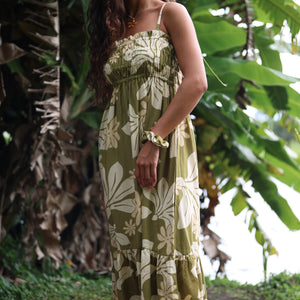 woman with brown hair wearing a maxi flowy dress in a green color with naupaka pattern throughout. 