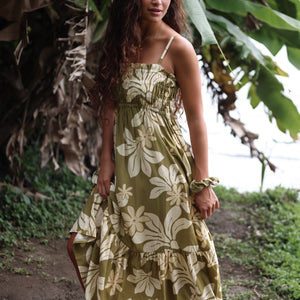 woman with brown hair wearing a maxi flowy dress in a green color with naupaka pattern throughout. 