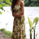 woman with brown hair wearing a maxi flowy dress in a green color with naupaka pattern throughout. 