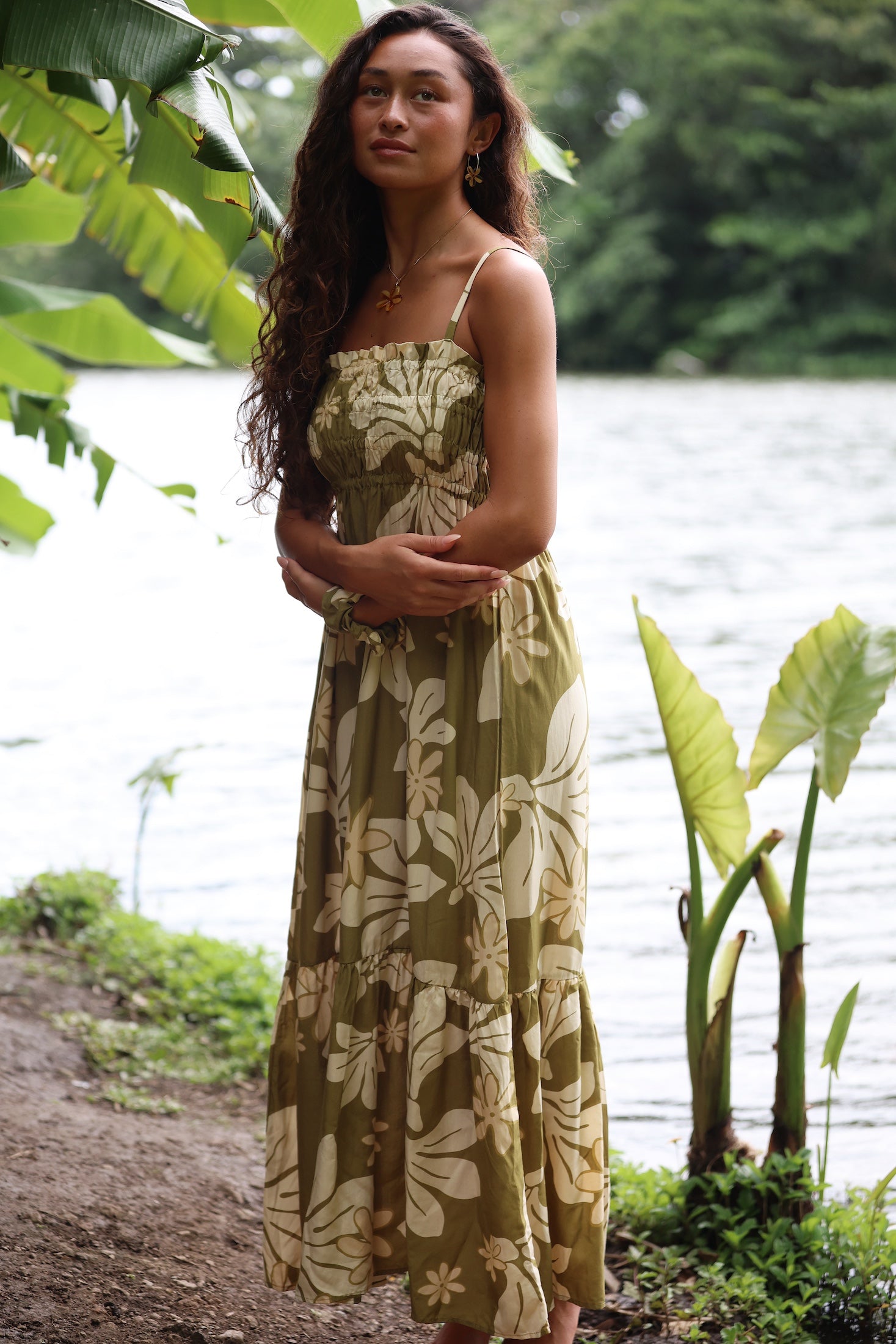 woman with brown hair wearing a maxi flowy dress in a green color with naupaka pattern throughout. 