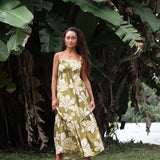 woman with brown hair wearing a maxi flowy dress in a green color with naupaka pattern throughout. 