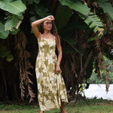 woman with brown hair wearing a maxi flowy dress in a green color with naupaka pattern throughout. 