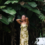 woman with brown hair wearing a maxi flowy dress in a green color with naupaka pattern throughout. 