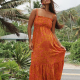 woman with brown hair wearing an orange long maxi dress with smocked bodice and spaghetti straps with puakenikeni print