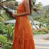 woman with brown hair wearing an orange long maxi dress with smocked bodice and spaghetti straps with puakenikeni print