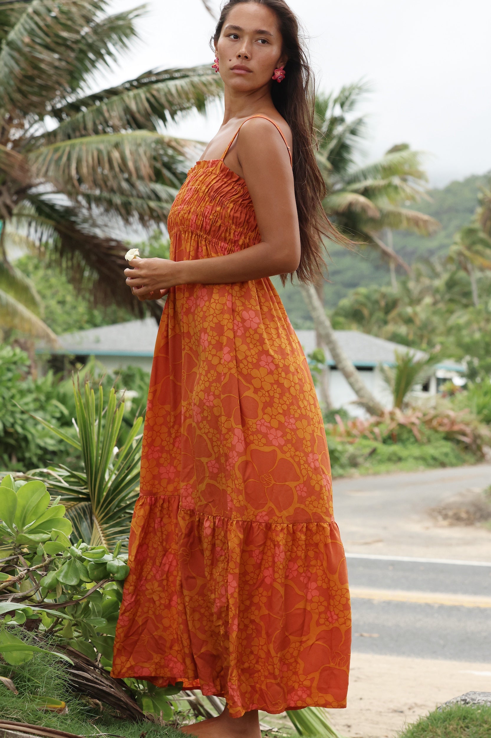 woman with brown hair wearing an orange long maxi dress with smocked bodice and spaghetti straps with puakenikeni print