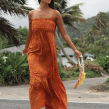 woman with brown hair wearing an orange long maxi dress with smocked bodice and spaghetti straps with puakenikeni print