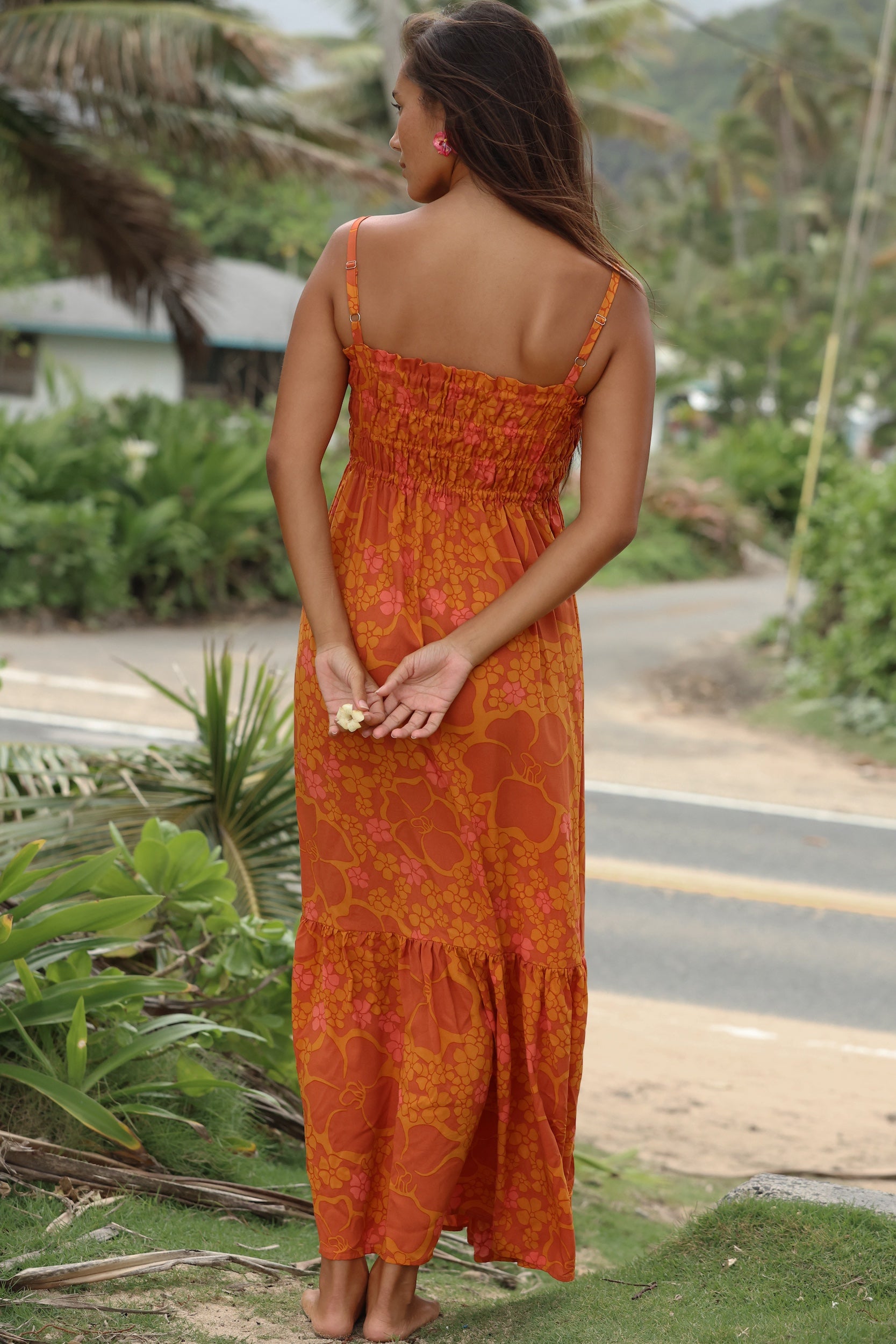 woman with brown hair wearing an orange long maxi dress with smocked bodice and spaghetti straps with puakenikeni print